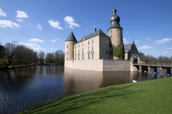 Das Wasserschloss Gemen in Borken mit Zwiebel-Erker und Brücke spiegelt sich an einem sonnigen Tag im weiten Graben. Eine grüne Wiese und Bäume rahmen das historische Schloss ein.