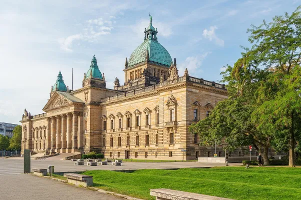Das historische Gebäude des Bundesverwaltungsgerichts in Leipzig mit kupfergrünen Kuppeln, Sandsteinfassade und grünem Vorplatz bei sonnigem Wetter.