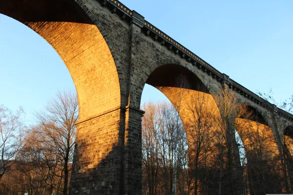 Froschperspektive auf die gewölbten Steinbögen der Parthe-Brücke. Das Mauerwerk wird von der tiefstehenden Sonne warm und goldgelb angestrahlt, dahinter stehen karge Winterbäume.