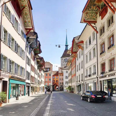 Blick durch eine Gasse der Altstadt von Aarau mit historischen Gebäuden, die für ihre kunstvoll bemalten Dachuntersichten bekannt sind. Im Hintergrund der Turm der Stadtkirche.